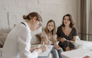A family doctor consults with a mother and daughter in a warm, welcoming medical office setting.
